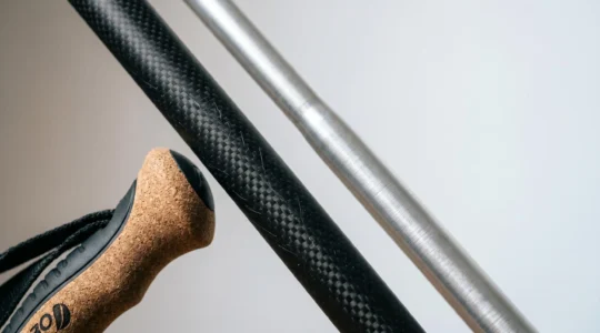 Close-up comparison of carbon fiber and aluminum walking pole shafts with ergonomic handles, showcasing material texture and grip design for arthritis relief